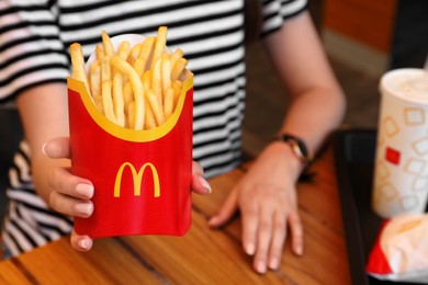 MYKOLAIV, UKRAINE - AUGUST 11, 2021: Woman with McDonald's French fries and drink at table in cafe, closeup