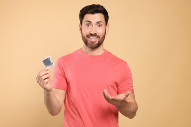 Photo of Confused man holding condom on beige background. Safe sex