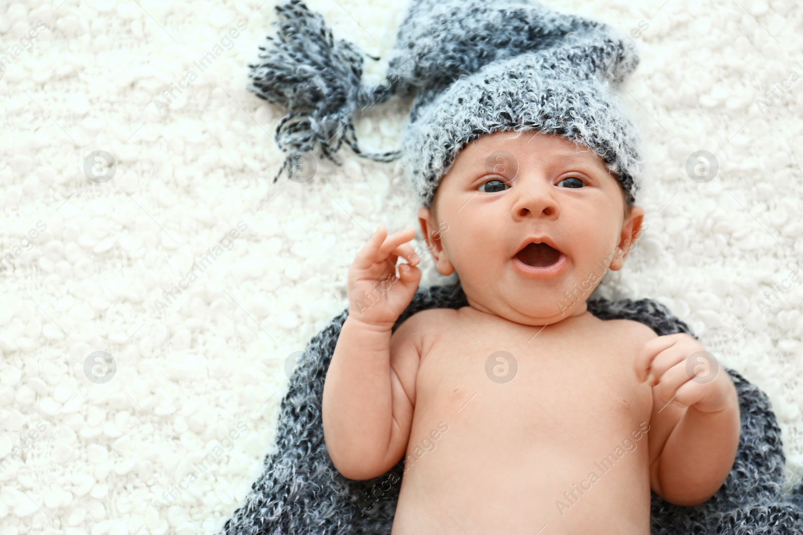 Photo of Cute little baby in grey hat and plaid lying on soft blanket, top view. Space for text