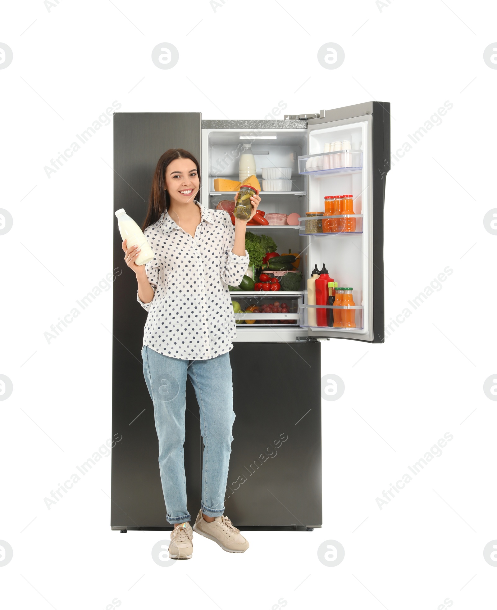 Photo of Young woman with milk and pickles near open refrigerator on white background