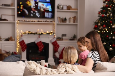 Photo of Happy mother with her children spending time near TV in cosy room. Christmas atmosphere