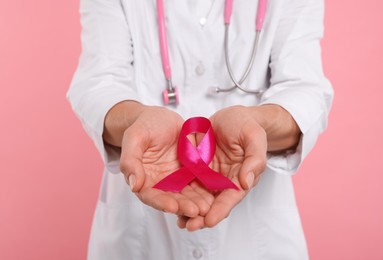 Photo of Doctor with stethoscope holding pink ribbon on color background, closeup. Breast cancer awareness