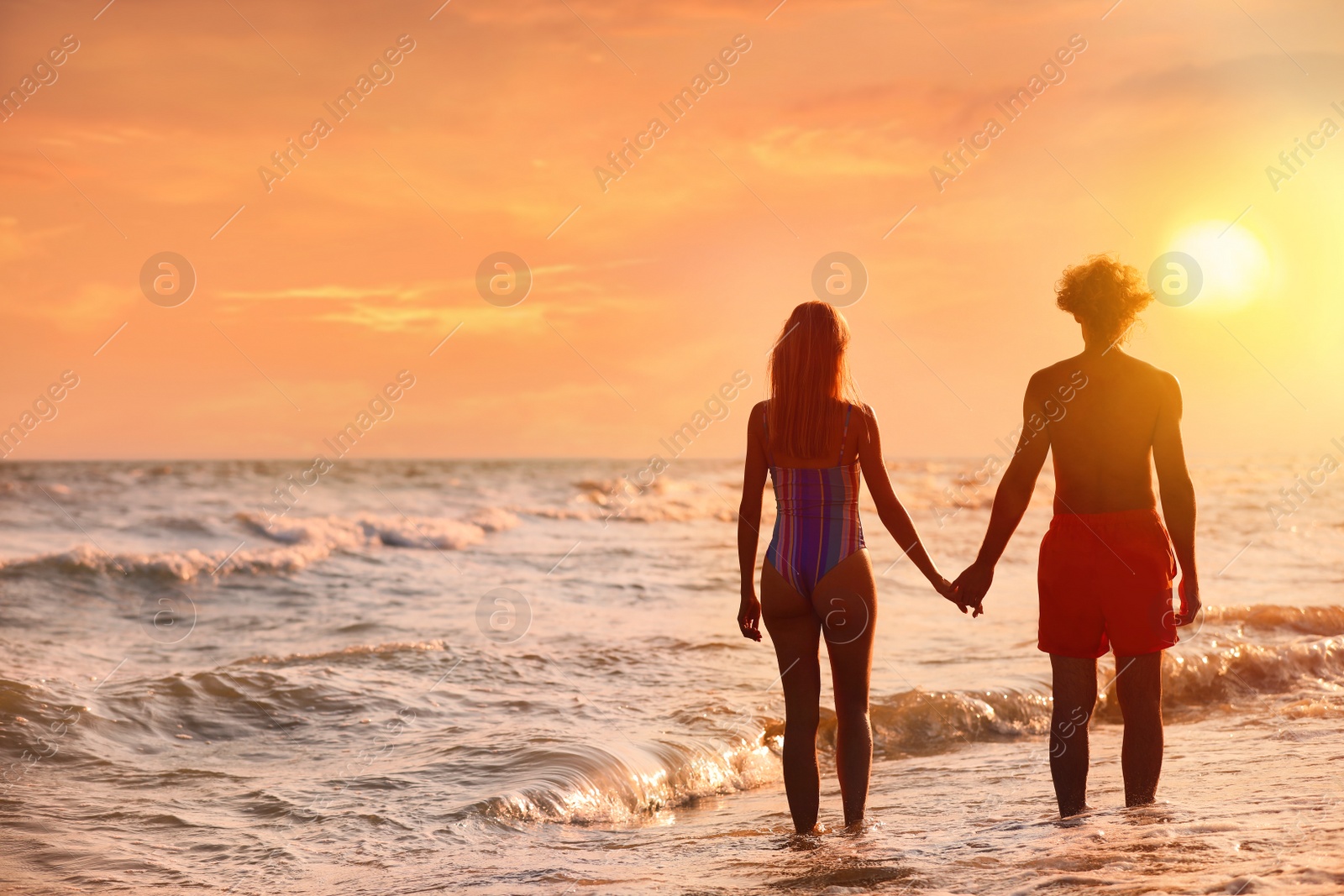 Photo of Young woman in bikini and her boyfriend on beach at sunset. Lovely couple