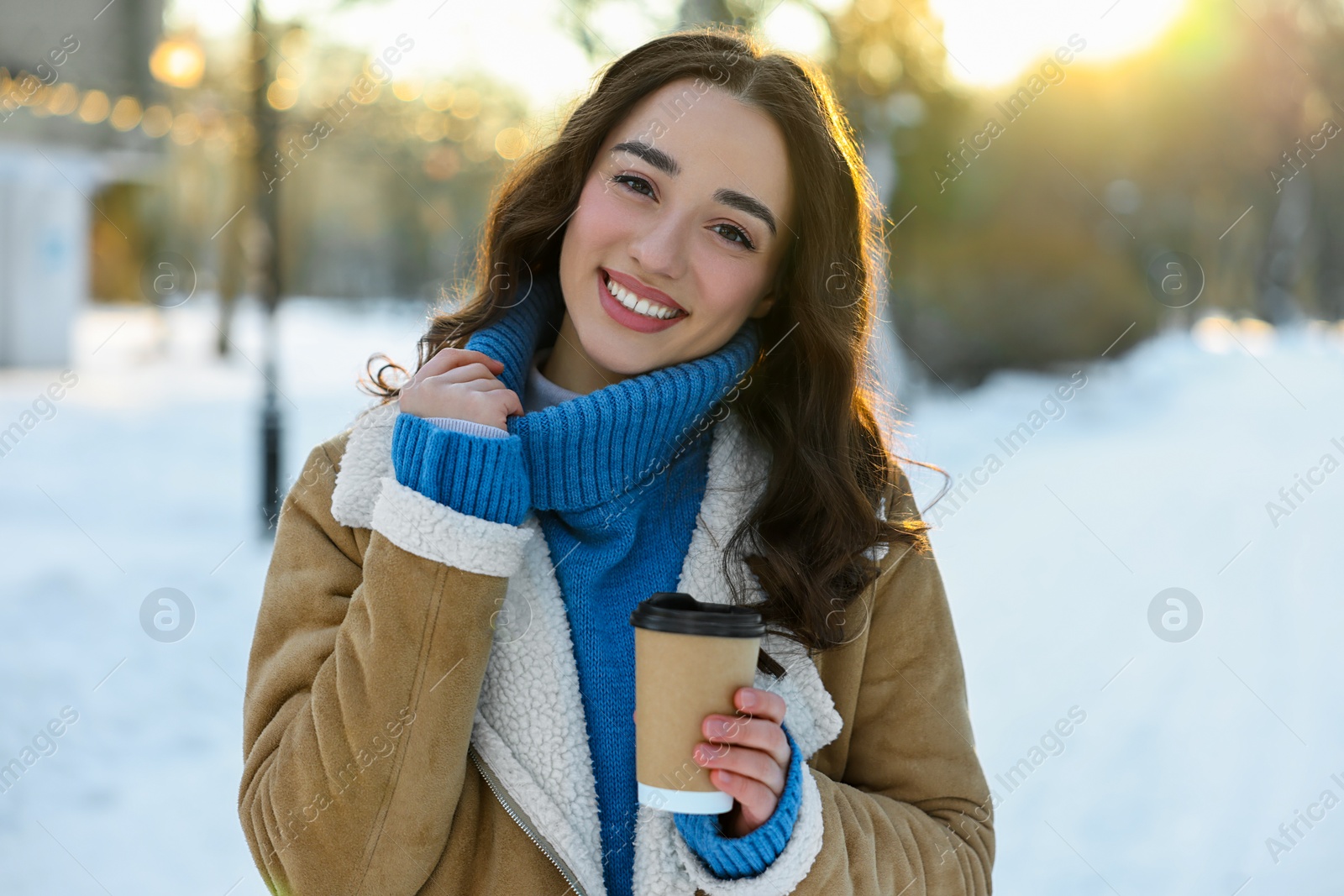 Photo of Portrait of smiling woman with paper cup of coffee in snowy park