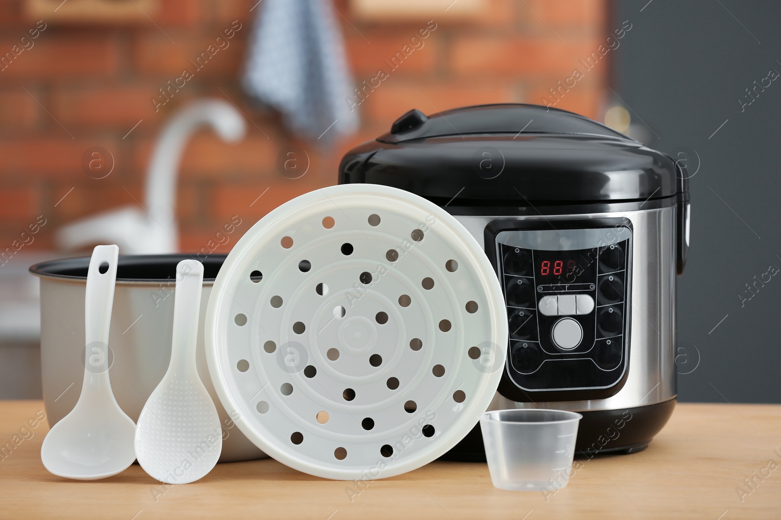 Photo of Modern electric multi cooker, parts and accessories on table in kitchen