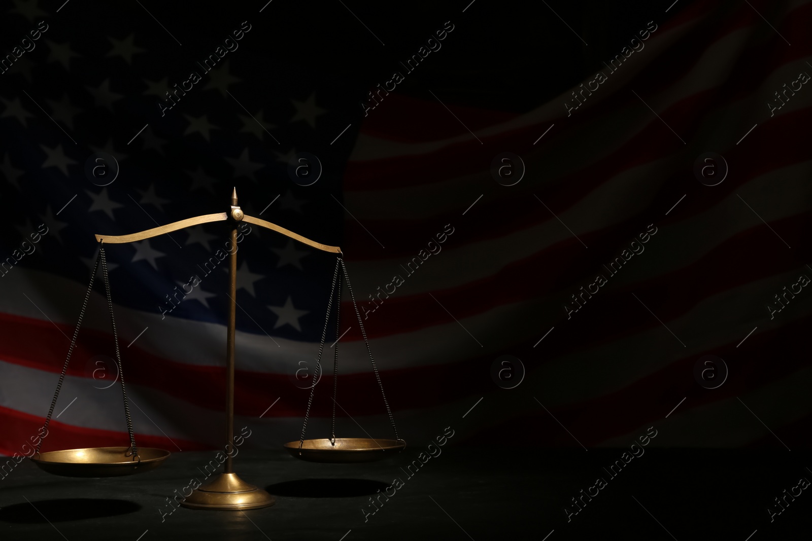 Photo of Scales of justice on black table against American flag in darkness, space for text