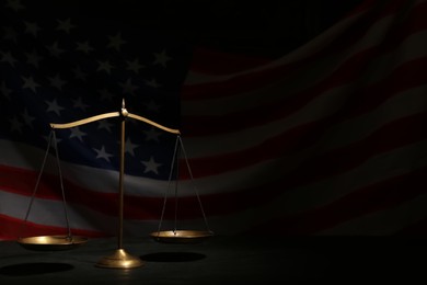 Photo of Scales of justice on black table against American flag in darkness, space for text