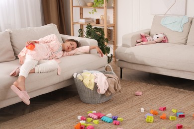 Tired young mother sleeping on sofa in messy living room