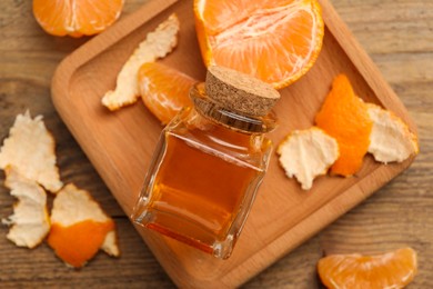 Photo of Bottle of tangerine essential oil and peeled fresh fruit on wooden table, top view