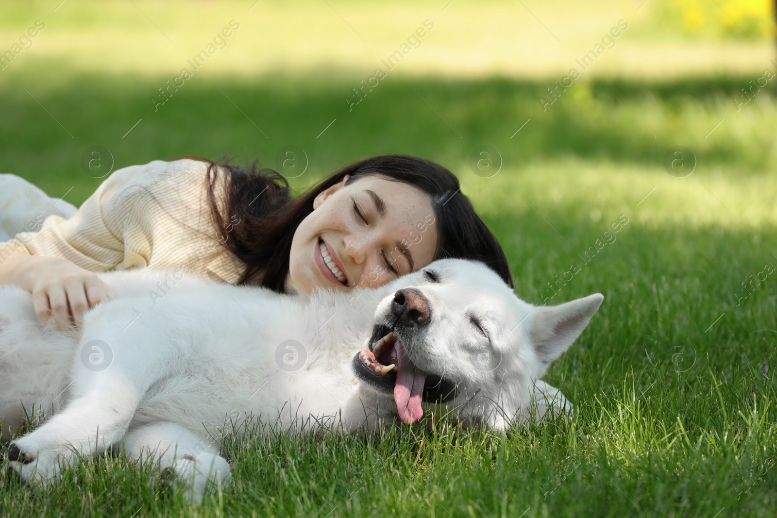 Photo of Teenage girl lying with her white Swiss Shepherd dog on green grass in park