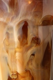 Glass of coffee with milk and ice cubes as background, closeup