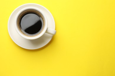 Fresh coffee in cup on yellow background, top view. Space for text