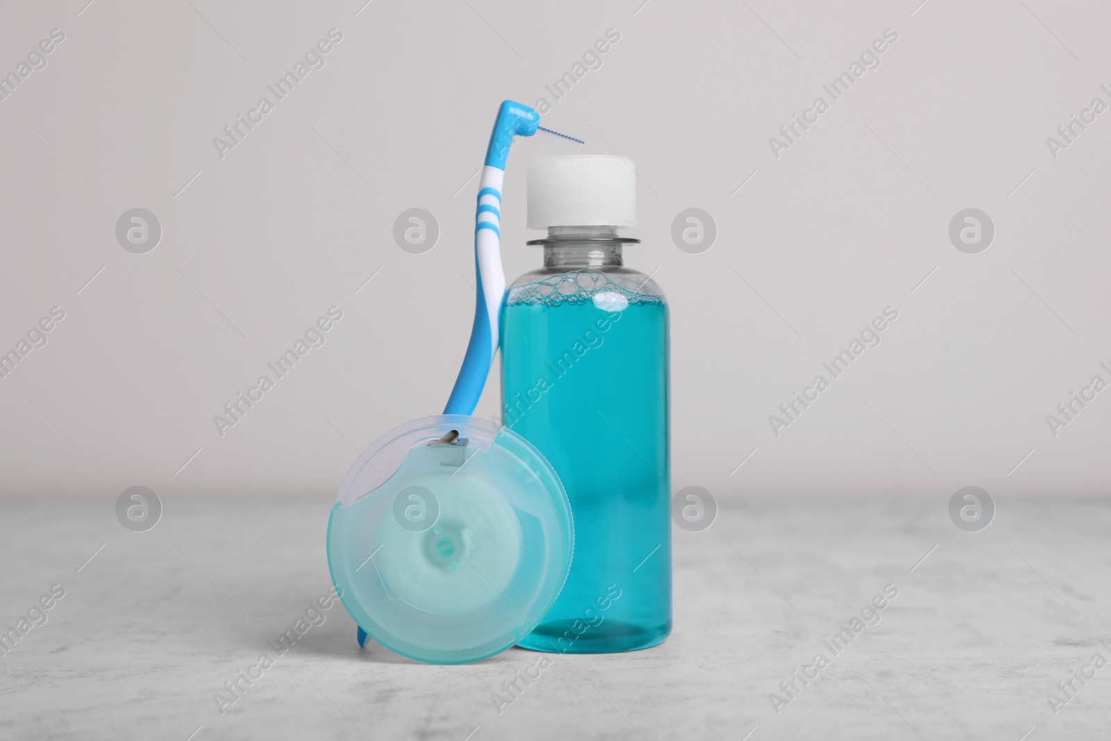 Photo of Dental floss and different teeth care products on light grey textured table