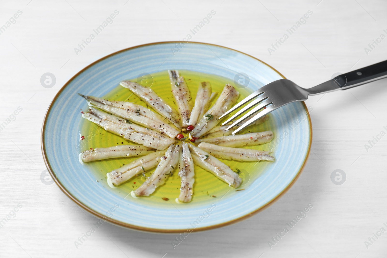 Photo of Tasty pickled anchovies with spices on white wooden table