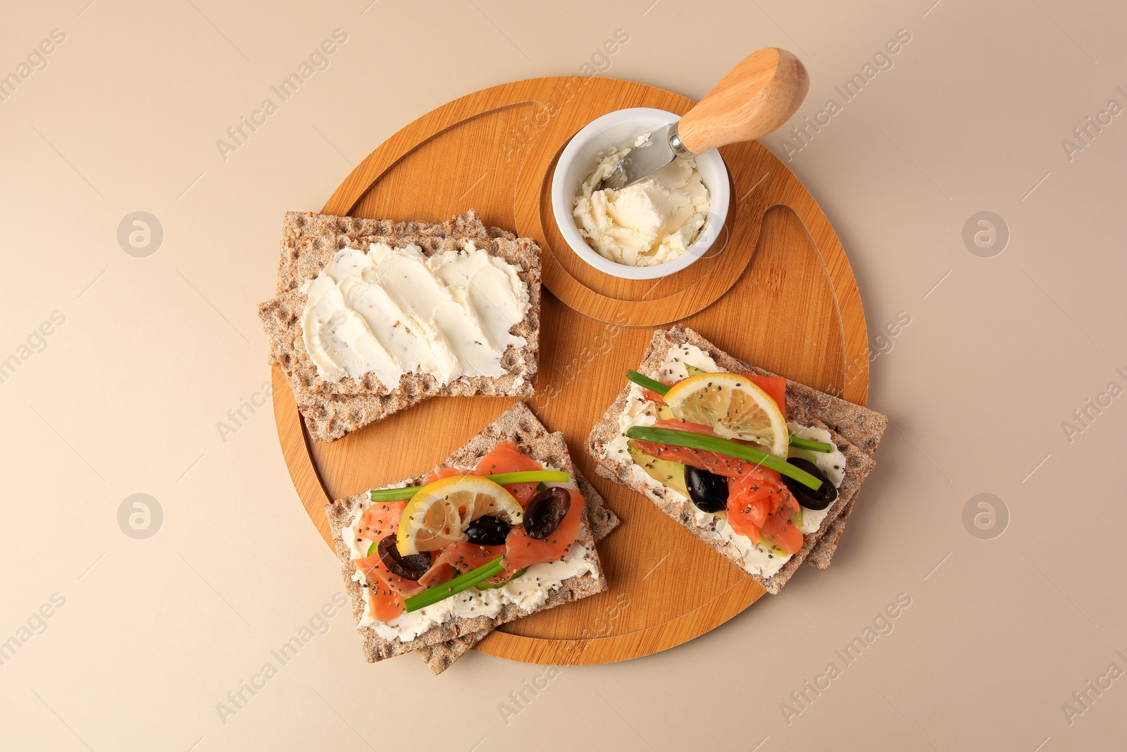 Photo of Fresh crunchy crispbreads with cream cheese, salmon, olives, lemon and green onion on beige background, top view