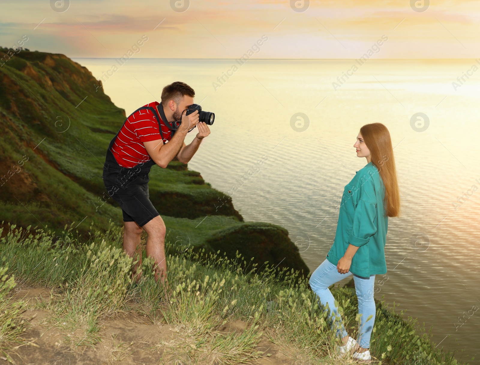 Photo of Male photographer taking picture of young woman with professional camera on green hill