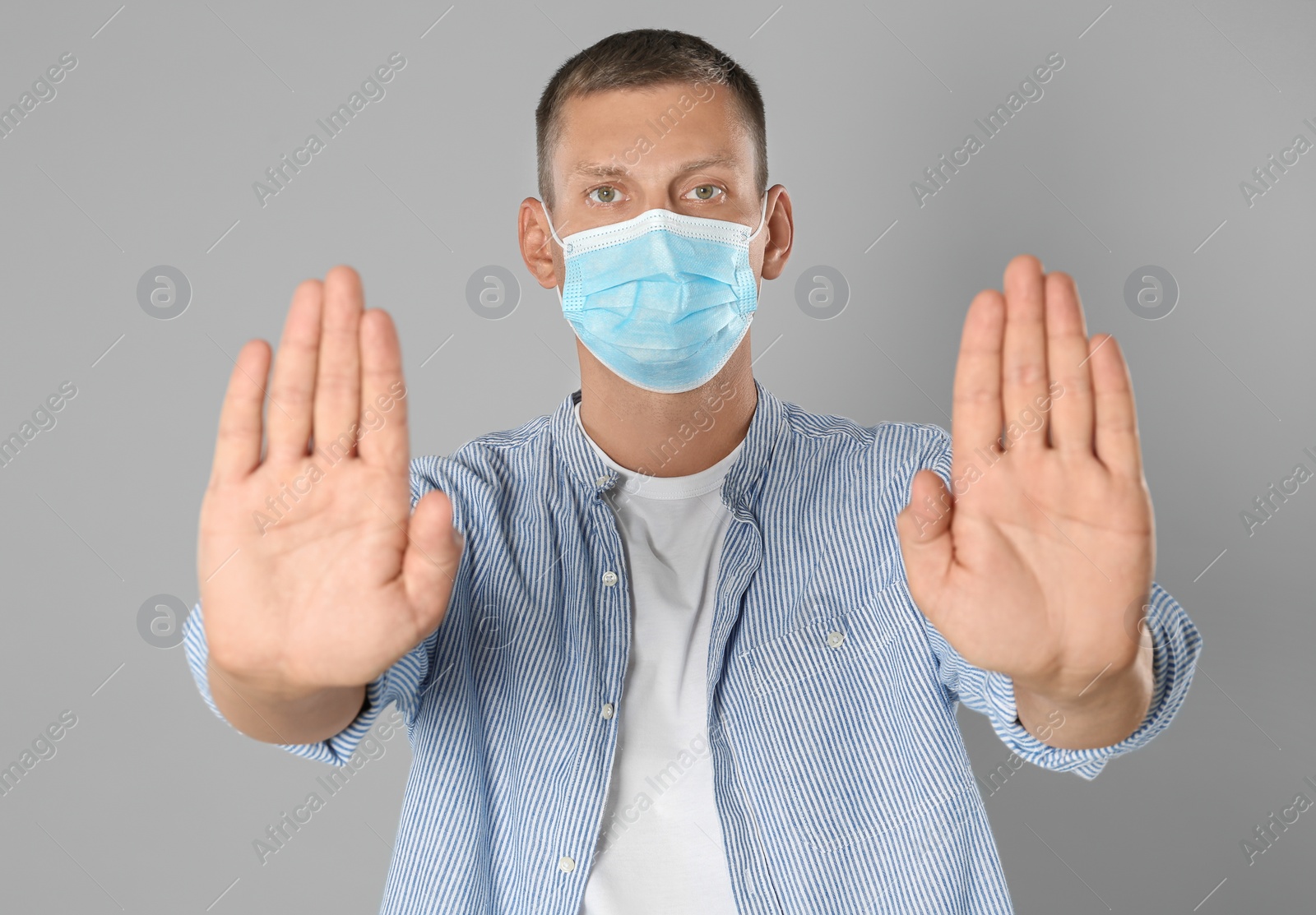 Photo of Man in protective mask showing stop gesture on grey background. Prevent spreading of coronavirus