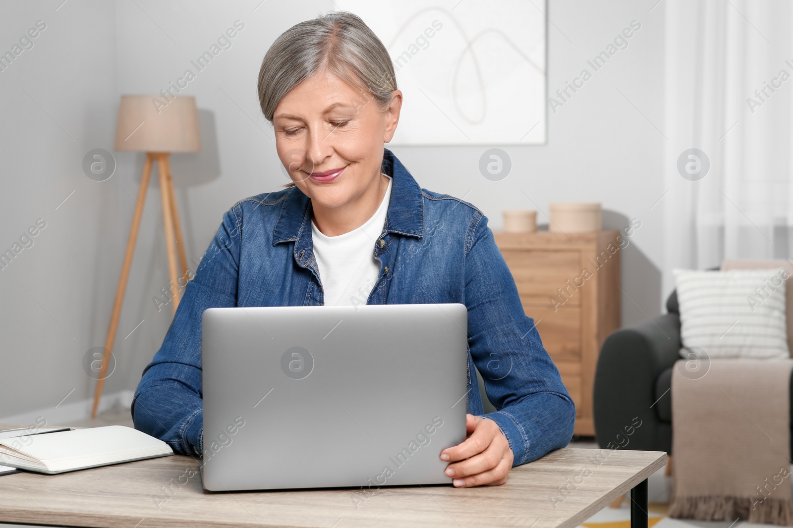 Photo of Beautiful senior woman using laptop at wooden table indoors