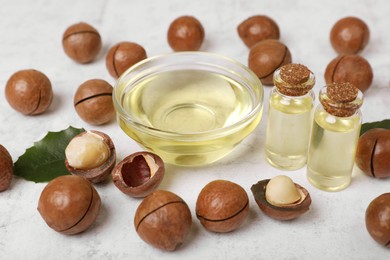 Photo of Delicious organic Macadamia nuts and natural oil on white textured table, closeup