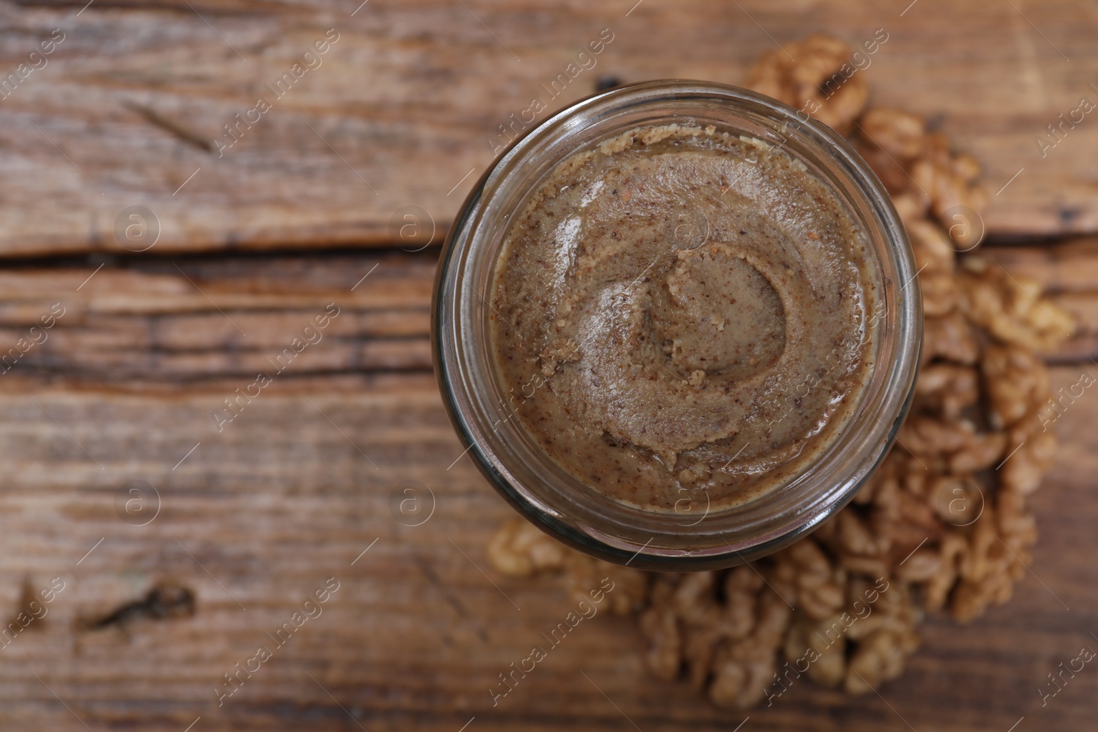 Photo of Tasty walnut nut paste in jar on wooden table, top view. Space for text