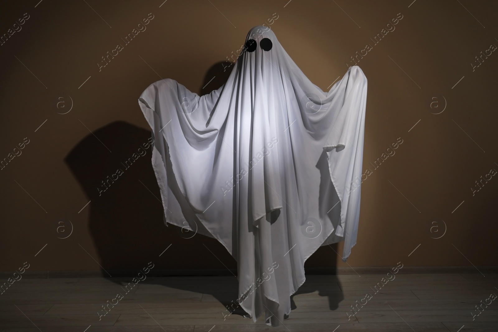 Photo of Creepy ghost. Woman covered with sheet near brown wall