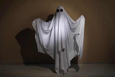 Photo of Creepy ghost. Woman covered with sheet near brown wall