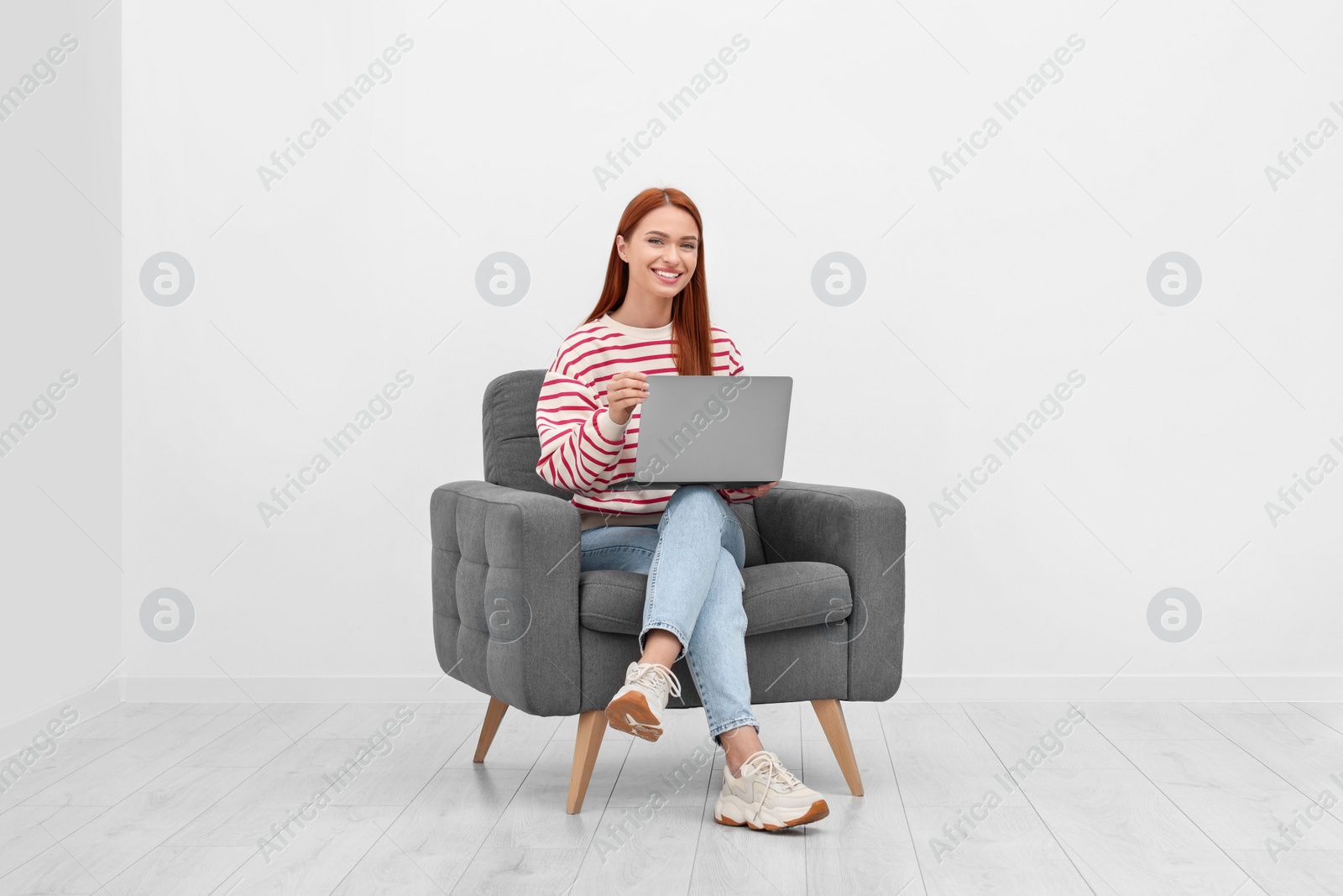 Photo of Happy young woman with laptop sitting in armchair near white wall indoors
