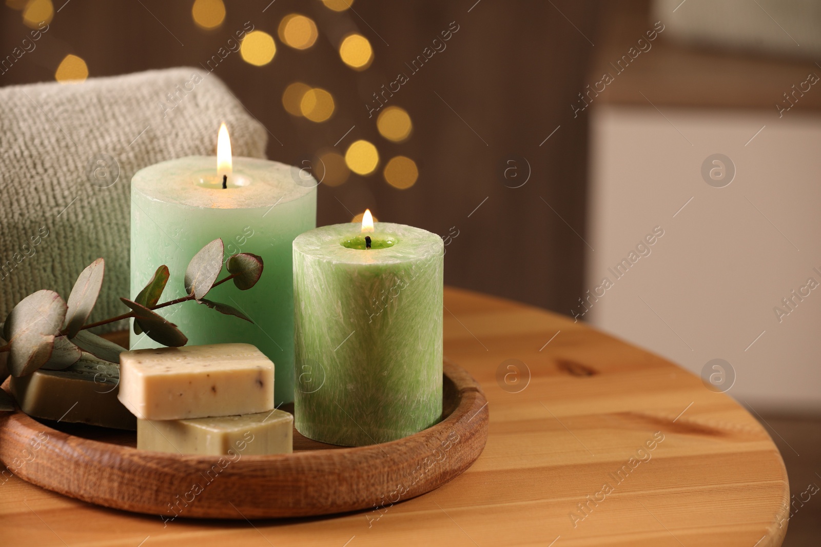 Photo of Spa composition. Burning candles, soap, towel and eucalyptus branch on wooden table, space for text