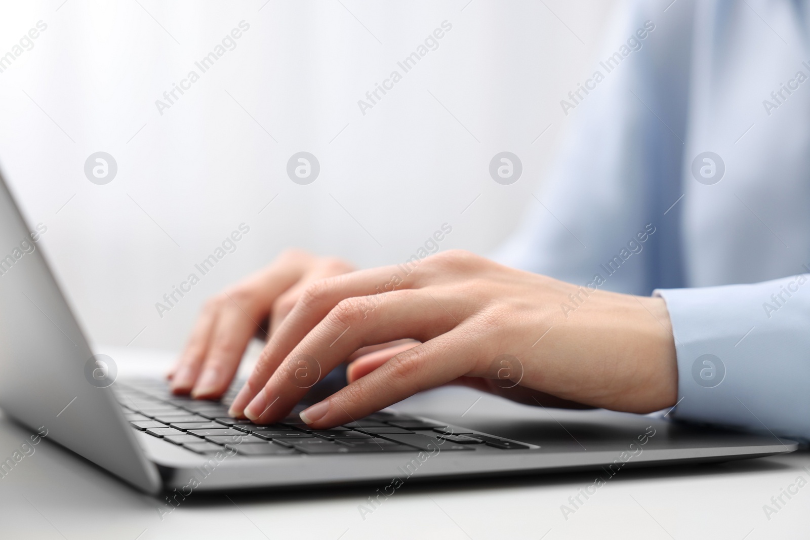 Photo of E-learning. Woman using laptop at white table indoors, closeup