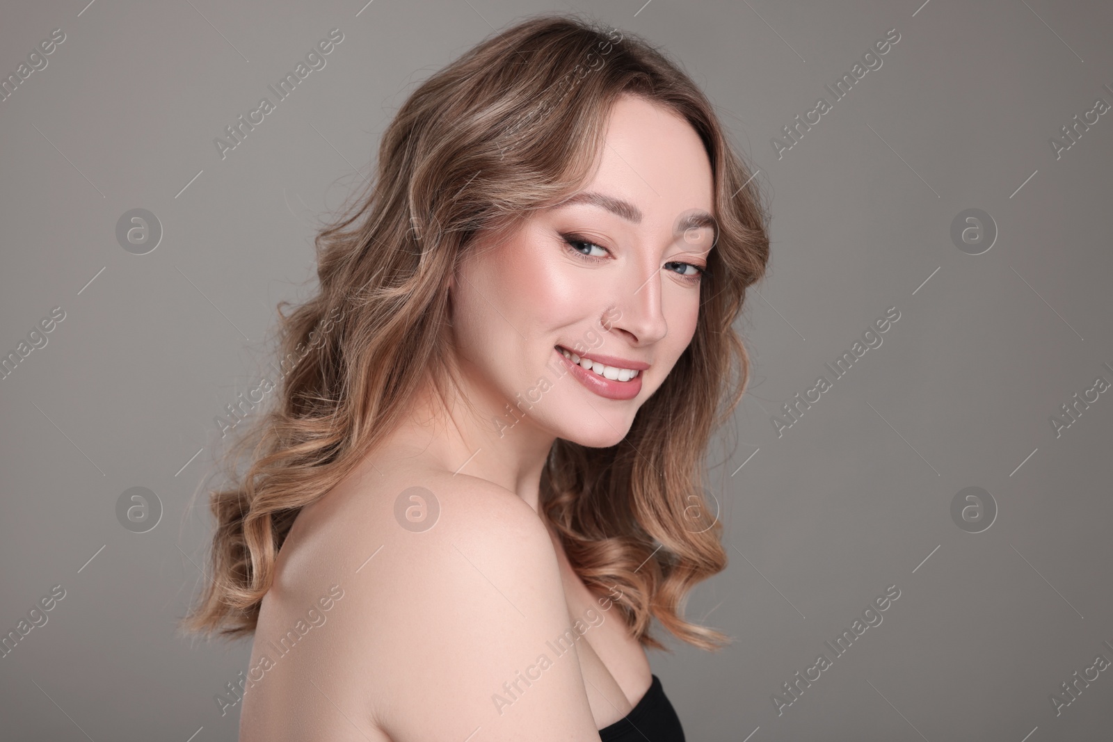 Photo of Portrait of smiling woman with curly hair on grey background