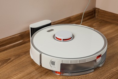 Photo of Robotic vacuum cleaner charging on wooden floor indoors