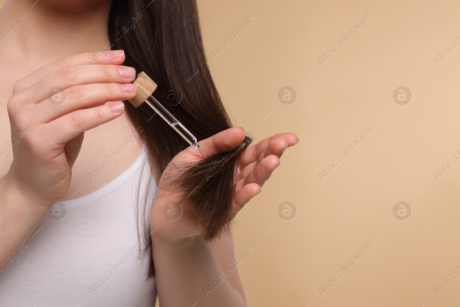 Photo of Woman applying essential oil onto hair on beige background, closeup and space for text