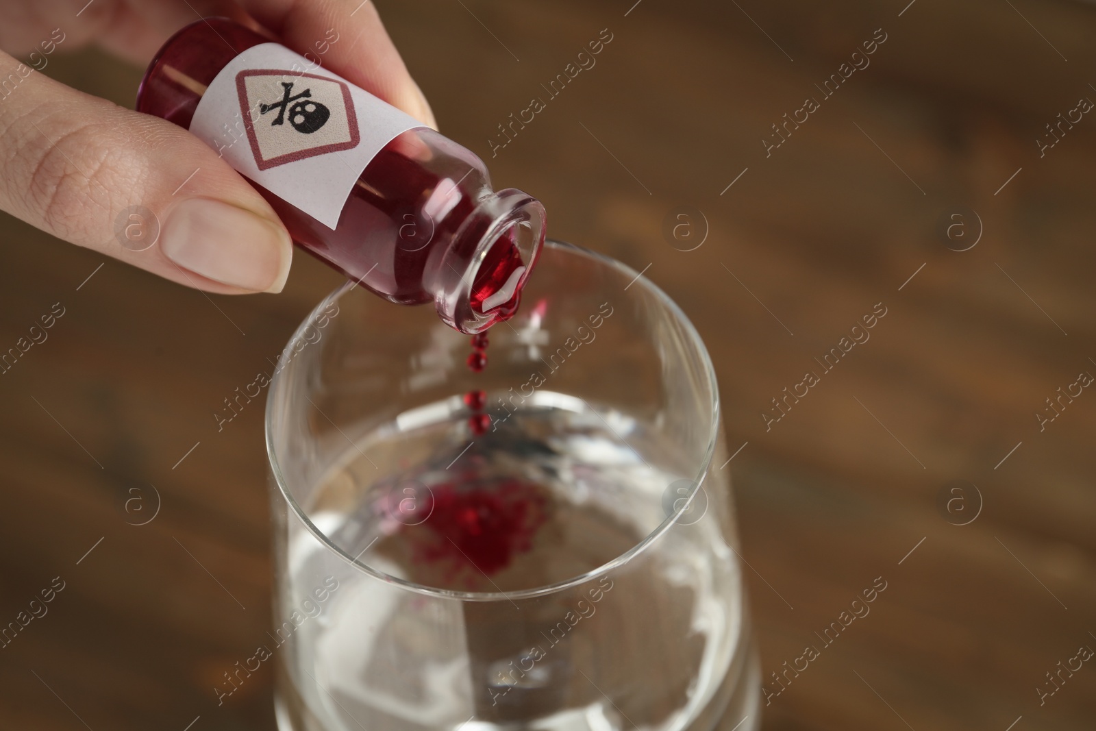 Photo of Woman pouring poison into glass of water on table, closeup