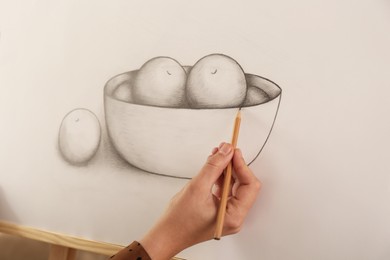 Photo of Woman drawing bowl of fruits with graphite pencil on canvas, closeup