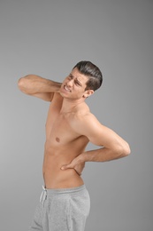 Young man suffering from back pain on grey background