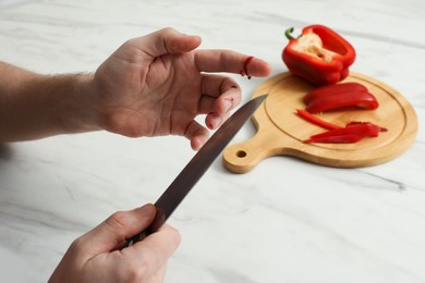 Photo of Man cut finger with knife while cooking at white marble table, closeup