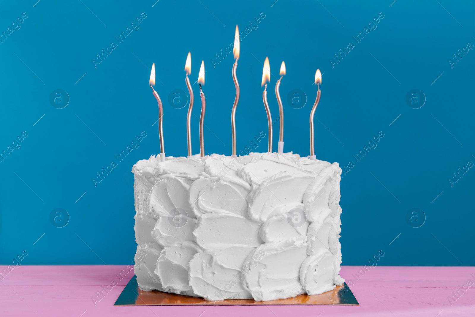 Photo of Delicious cake with cream and burning candles on pink wooden table