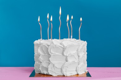 Photo of Delicious cake with cream and burning candles on pink wooden table