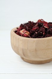 Photo of Hibiscus tea. Bowl with dried roselle calyces on white wooden table, closeup