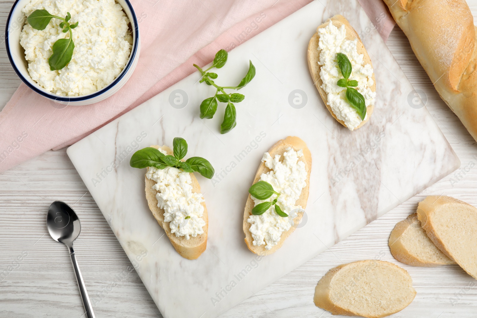 Photo of Bread with cottage cheese and basil on white wooden table, flat lay