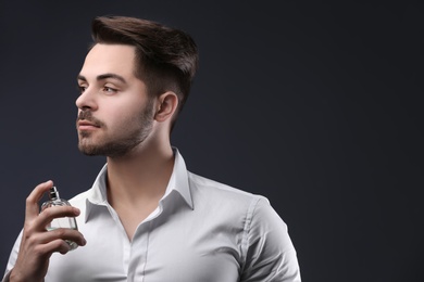 Handsome man in shirt using perfume on dark background