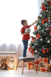 Cute little child standing on stool and decorating Christmas tree at home