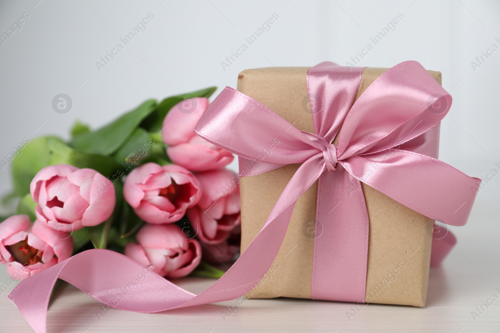 Photo of Beautiful gift box with bow and pink tulip flowers on light table, closeup