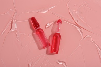 Skincare ampoules on pink surface with gel, top view