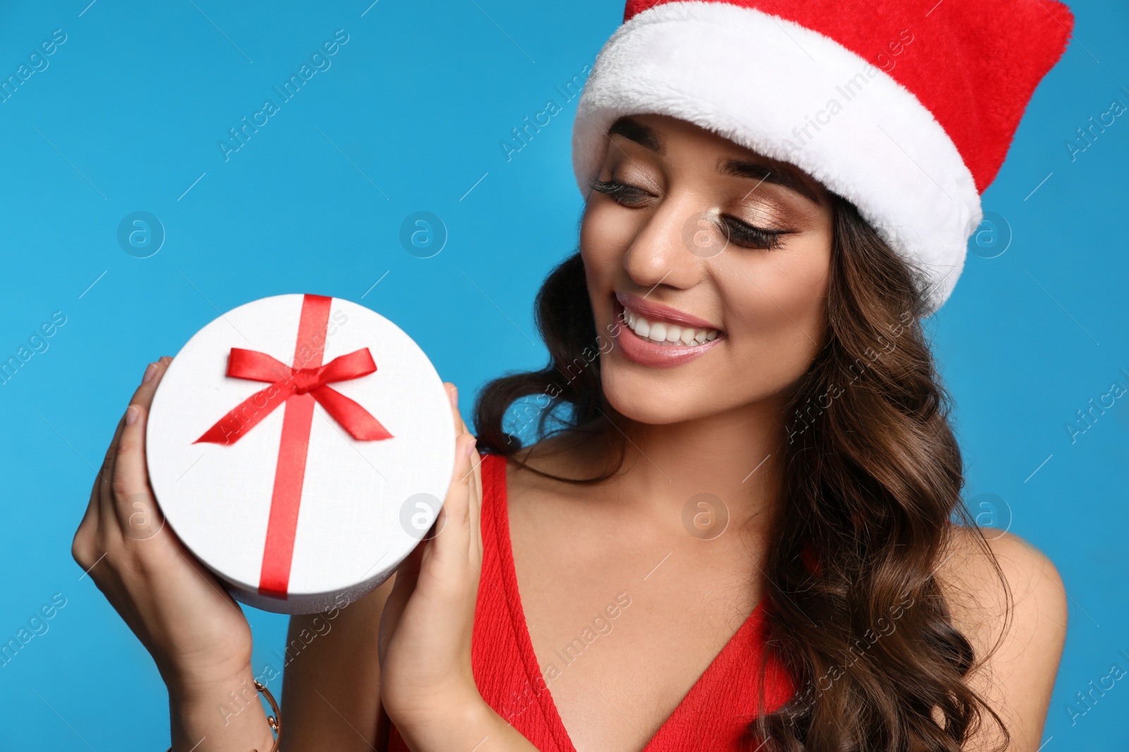 Photo of Beautiful woman in Santa hat with Christmas gift on blue background