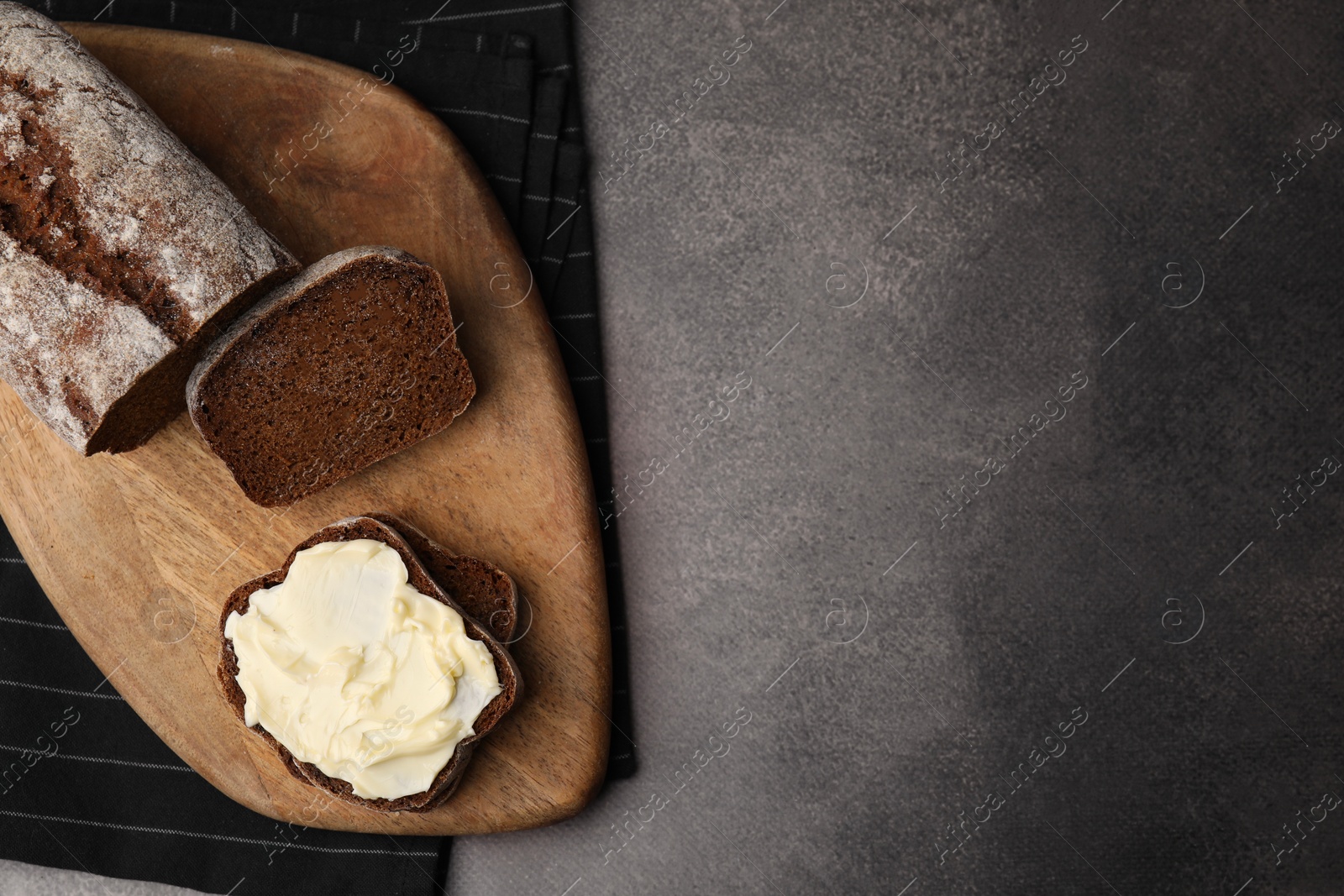 Photo of Tasty bread with butter on grey textured table, top view. Space for text