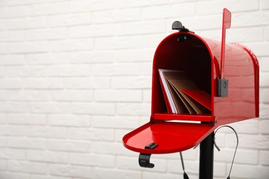 Photo of Open red letter box with envelopes near white brick wall. Space for text