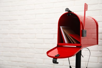 Open red letter box with envelopes near white brick wall. Space for text