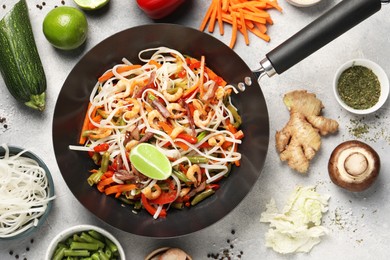 Photo of Shrimp stir fry with noodles and vegetables in wok surrounded by ingredients on grey table, flat lay