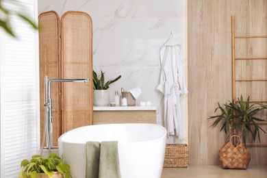 Modern white tub and beautiful green houseplants in bathroom. Interior design